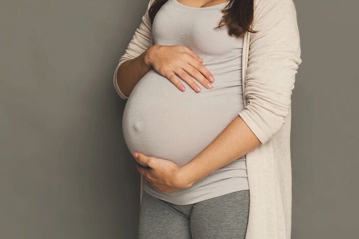 pregnant woman in tan with brown hair holding her round belly